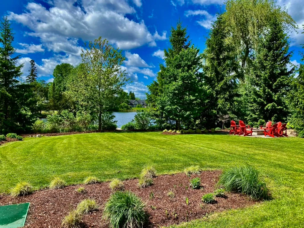 Backyard lawn, garden beds and a pond with Muskoka chairs